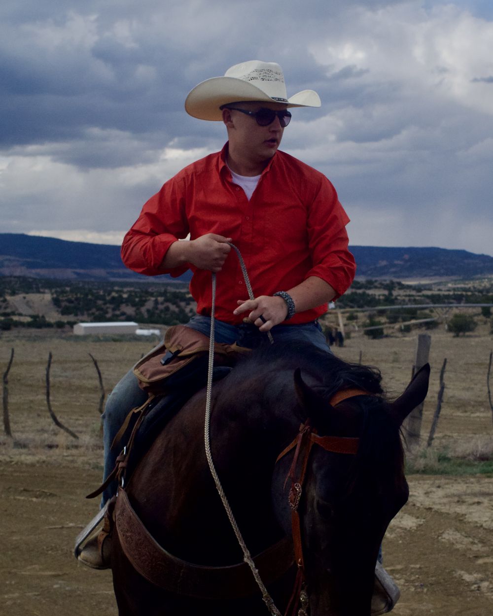 Daniel Wells in a white cowboy hat and red shirt on horseback