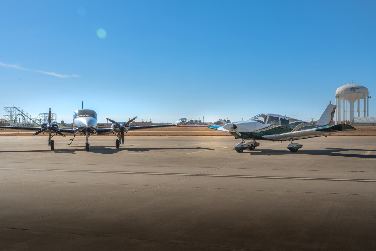 A twin-engine airplane and a Piper Cherokee parked side by side on the ramp