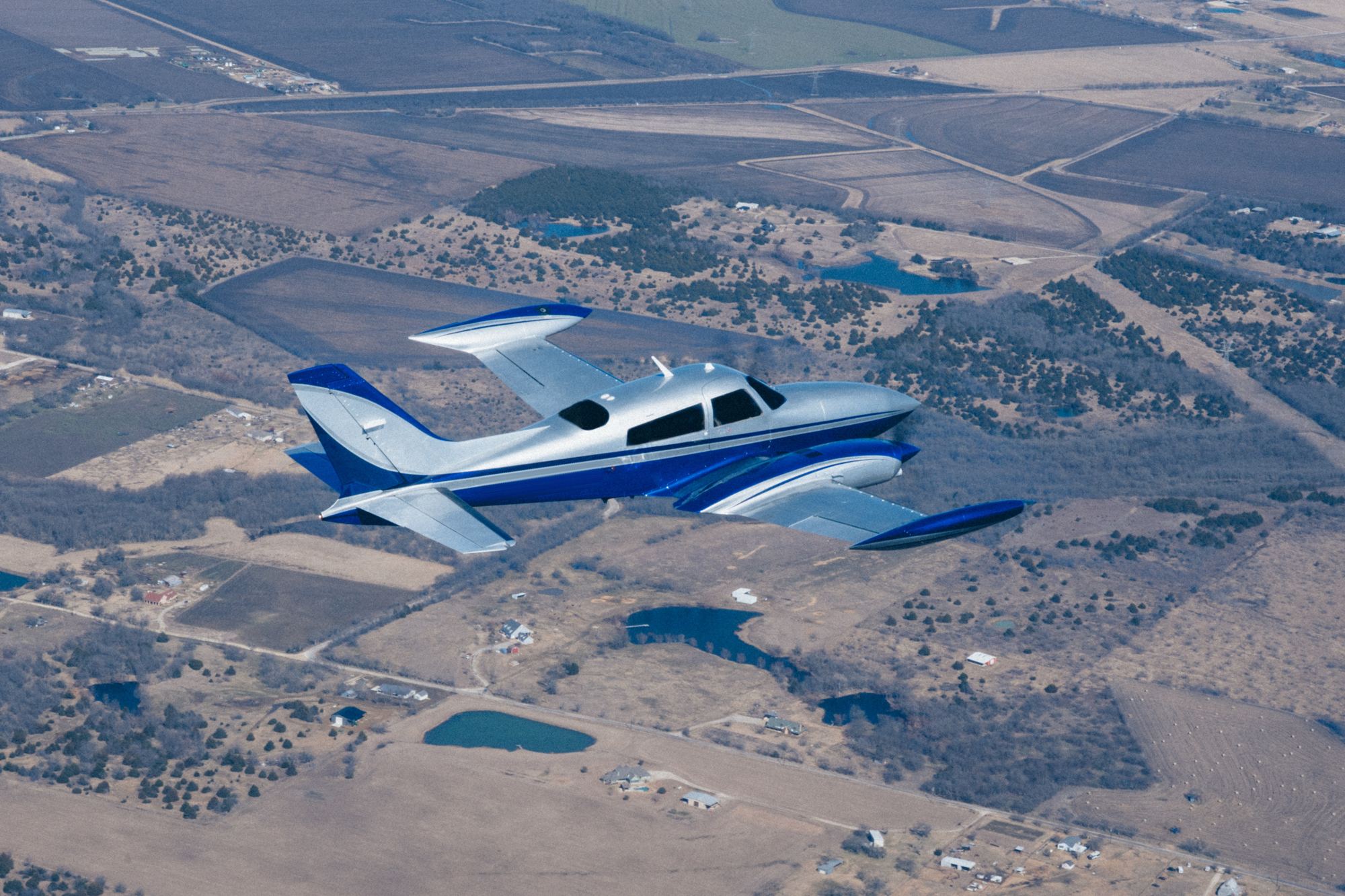 Navy and silver twin-engine airplane in flight over Texas farmland